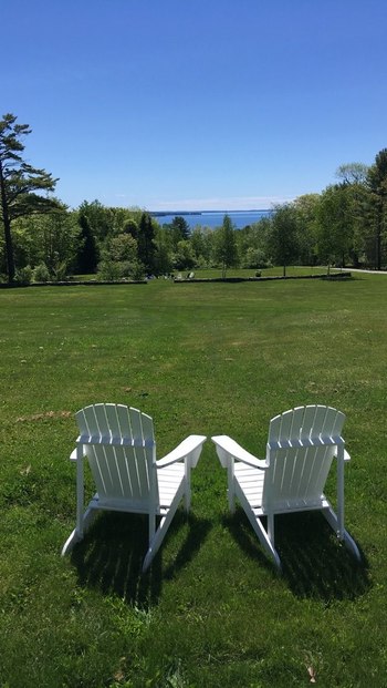 two white lawn chairs ongreen lawn looking towards distant ocean view